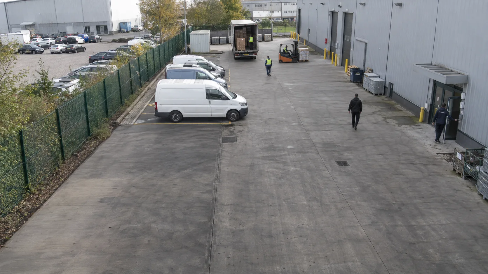 Distribution centre apron with parked vehicles, staff entrance and an adjacent car park.